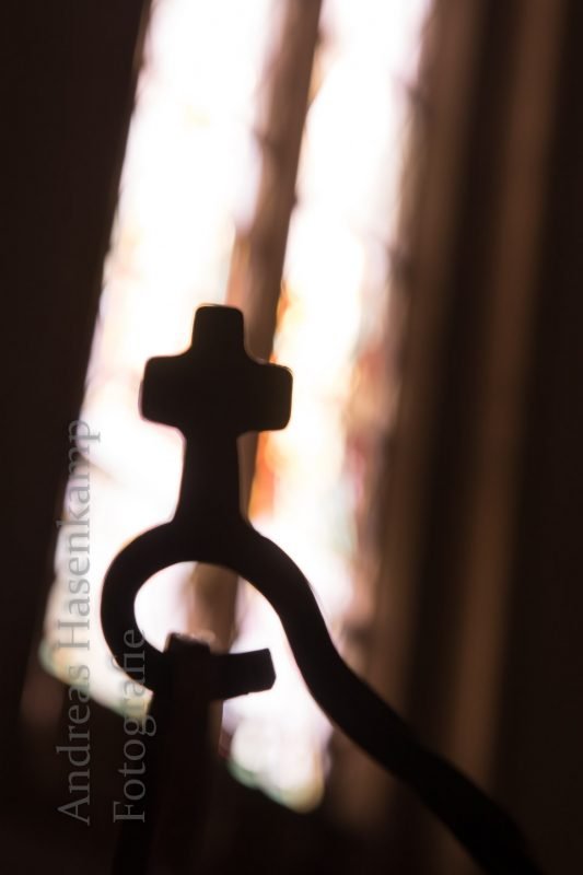 Kreuz am Weihwasser-Halter im Gegenlicht des Kirchenfensters